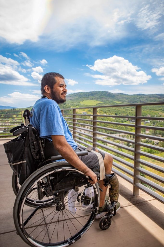 Hombre en silla de ruedas con prótesis en la pierna disfrutando de las vistas de la montaña en un día soleado.