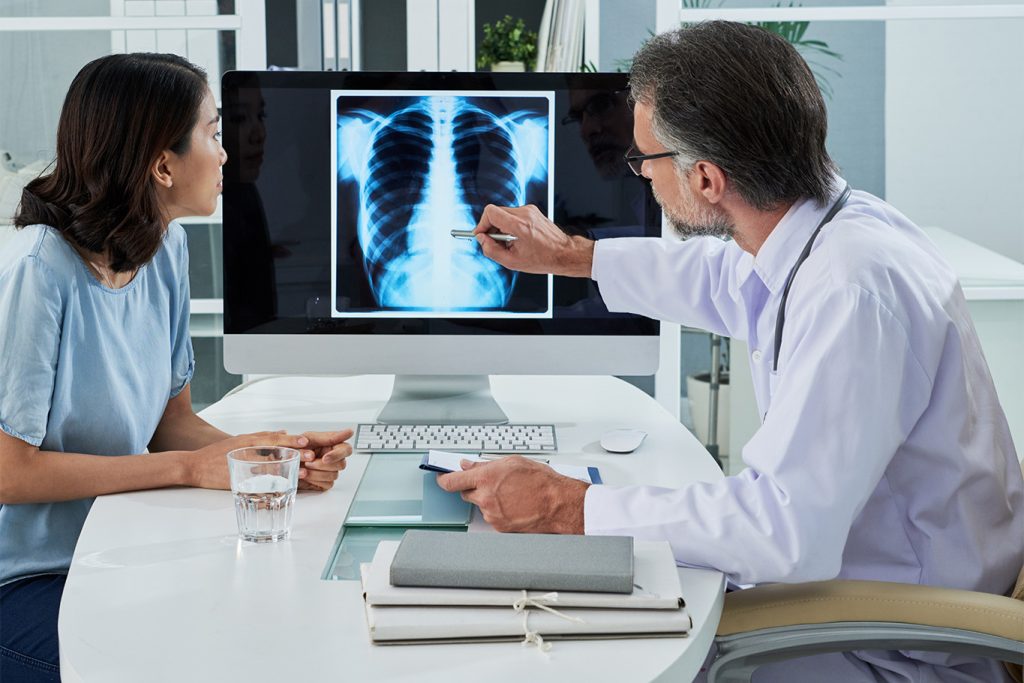Doctor explains chest X-ray results to a patient on a computer screen in a medical office.