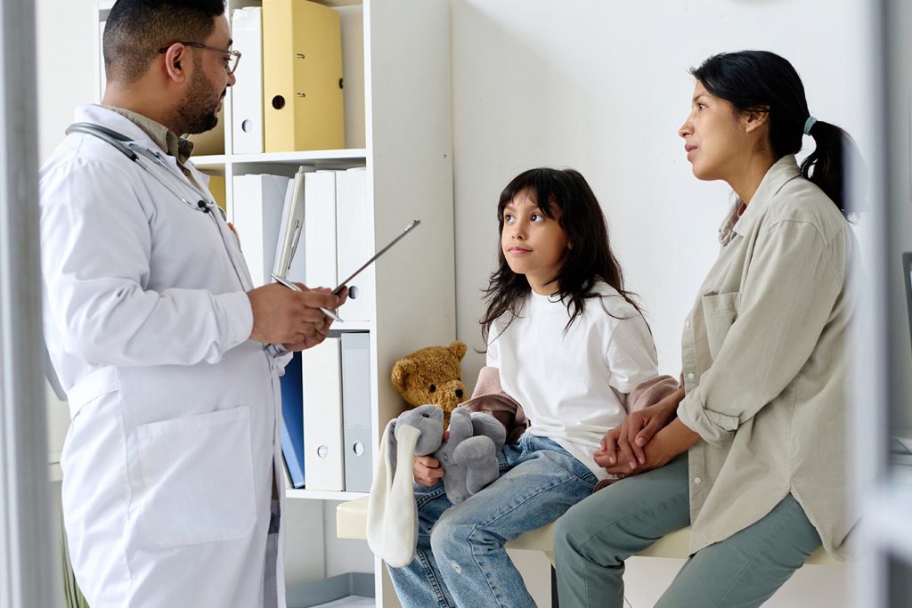 Doctor in discussion with a child holding a stuffed toy and a woman at a medical appointment.