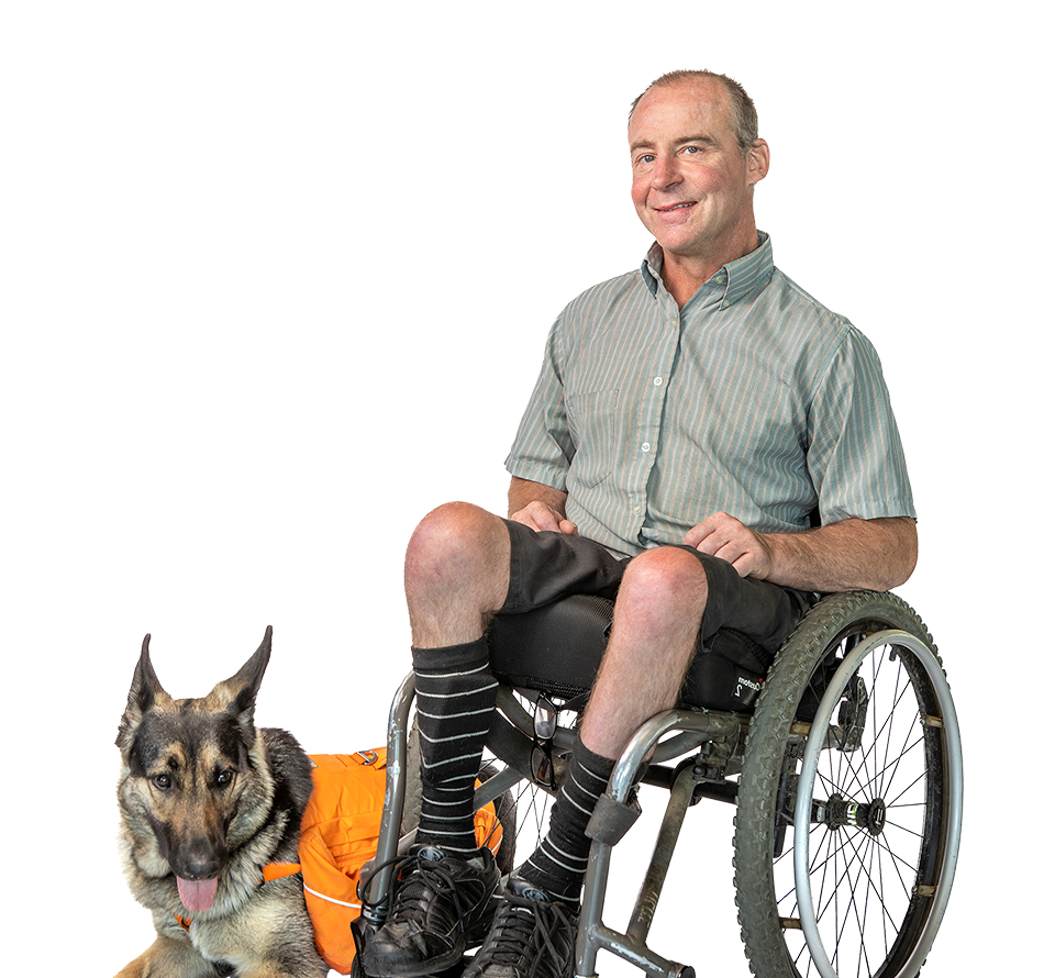 Hombre en silla de ruedas con su perro de asistencia a su lado, ambos sonriendo, reforzando el trabajo en equipo y la asistencia.