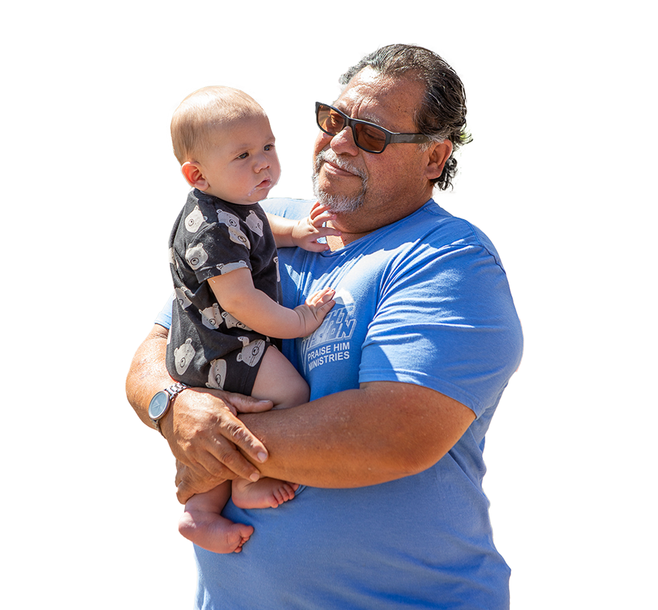 Grandfather in sunglasses holding baby in printed outfit, sharing a joyful outdoor moment.