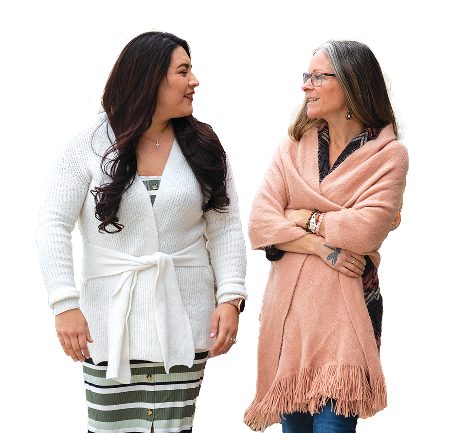 Two women in cozy cardigans chatting amicably, one in white and one in pink, enjoying a friendly conversation outdoors.