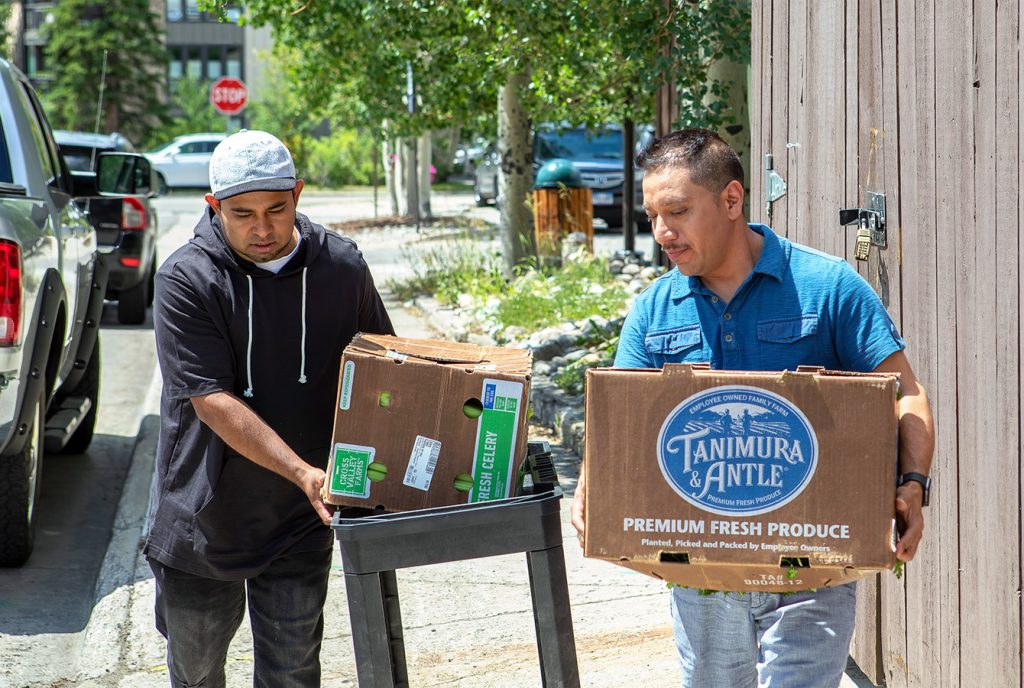 Two men transporting boxes of fresh produce outdoors. Labels show Tanimura & Antle and Fresh Celery.