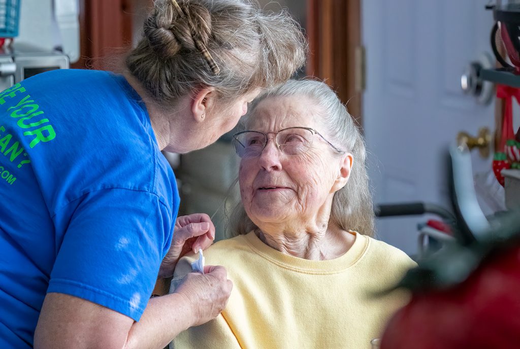 Caregiver assists smiling elderly woman at home, promoting companionship and healthcare support.