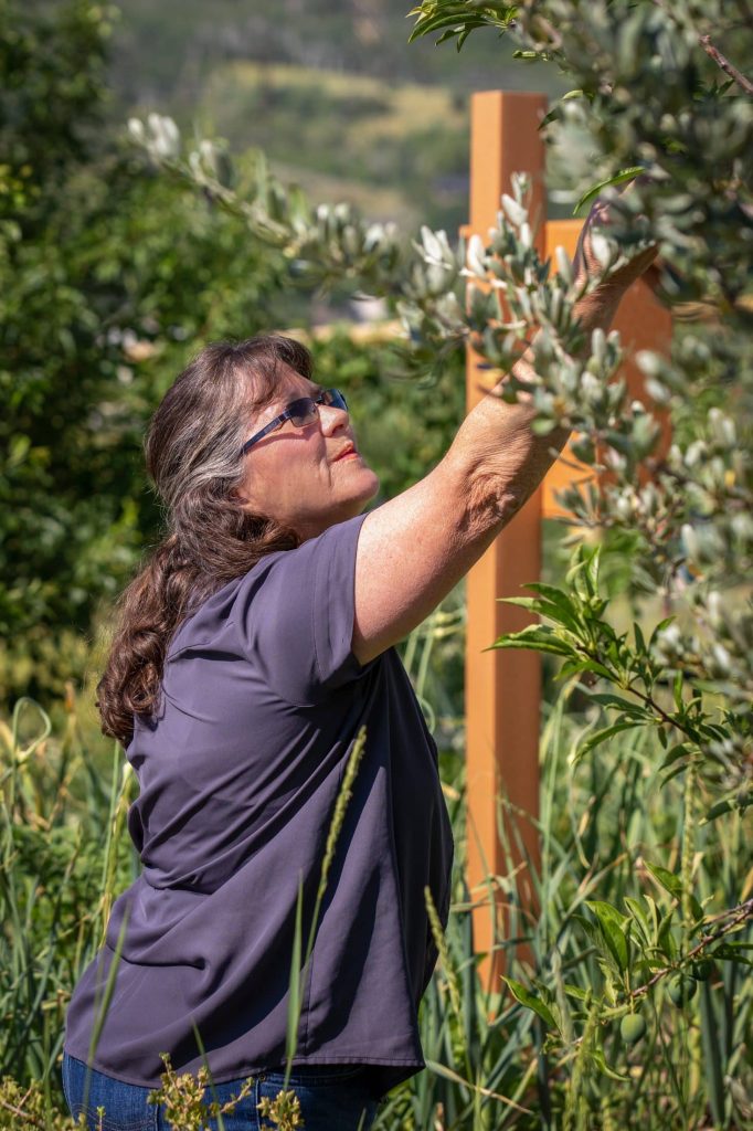 Woman reaching for leaves in a sunny garden, surrounded by green foliage and nature.