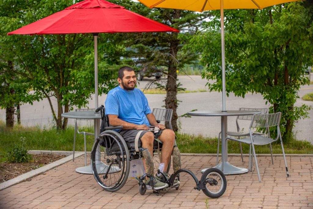 Man in wheelchair enjoying outdoor patio area with colorful umbrellas and greenery.