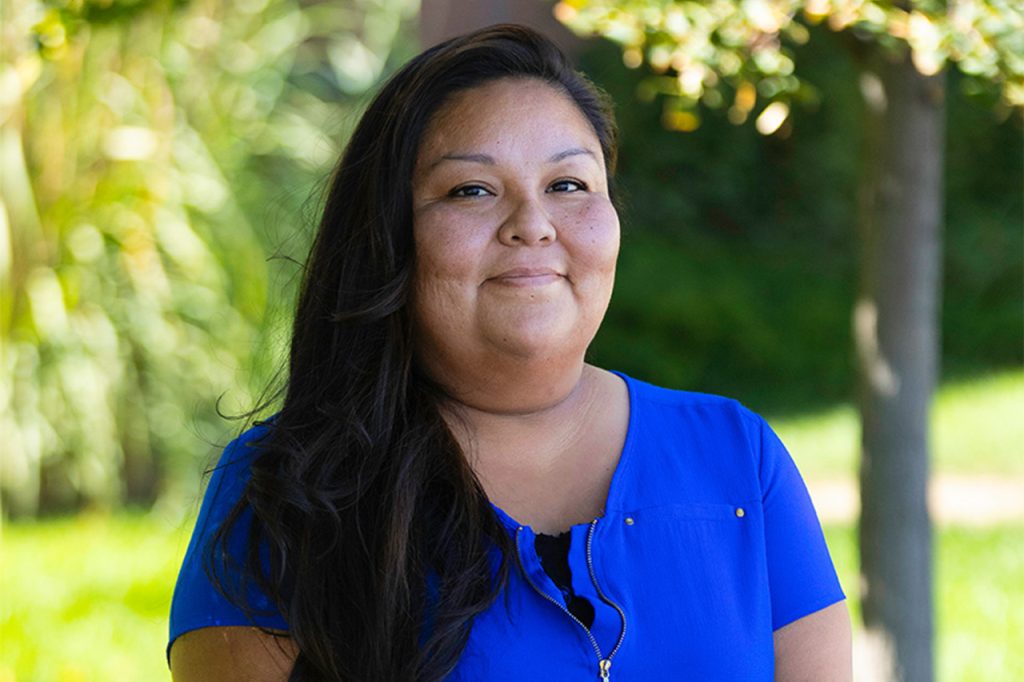 Smiling woman in blue shirt outdoors with green blurred background.