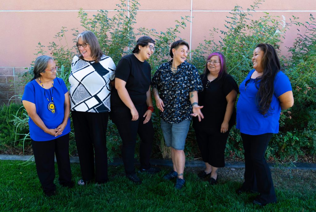 A group of six people laughing and chatting outdoors near a hedge, showcasing diversity and friendship.