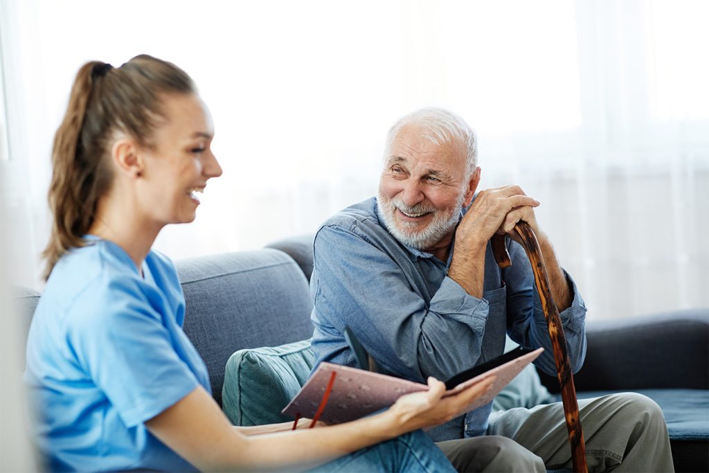 A home health professional reviews a medical chart with a senior man at his home.
